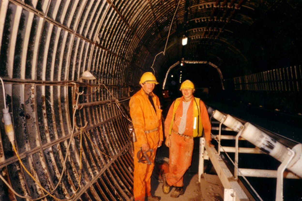 Two men in orange hi-vis overalls stand in an enormous dark tunnel